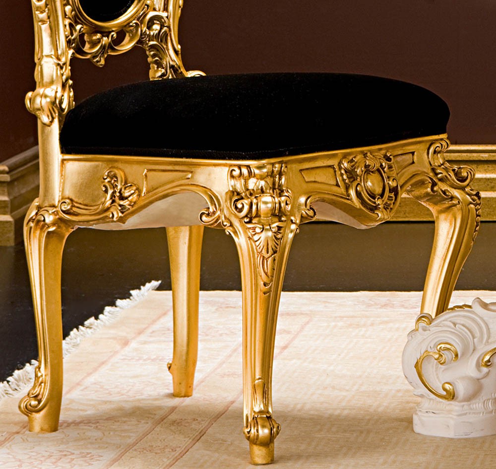 Decorative gold chair with black cushion on a patterned floor.