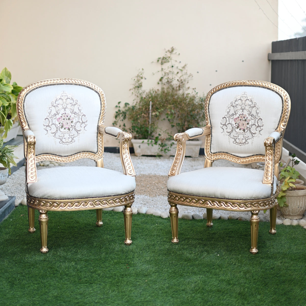 Pair of ornate chairs with gold frames and white cushions on a grassy area.