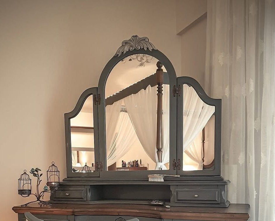 Tri-fold mirror on a wooden dresser with decorative elements in a room setting.