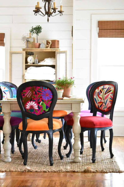 A dining set featuring a white distressed French finish table and black dining chairs with floral fabric upholstery, arranged in a room with a light wooden floor and a white ceiling.