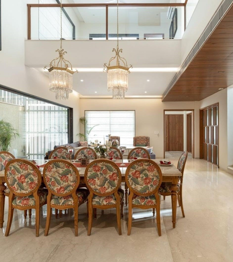 A luxurious dining room featuring a large rectangular Italian marble tabletop with a floral patterned dining set, including chairs and a chandelier.