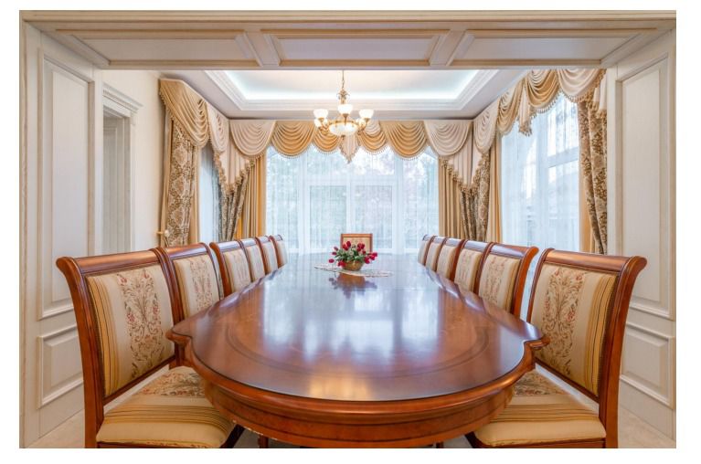 A luxurious 10-seater dining set made of teak wood with a carved top design and plush beige upholstered chairs, displayed in an elegantly decorated dining room.