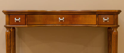 Wooden console table with three drawers against a beige wall