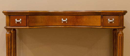 Wooden console table with three drawers against a beige wall