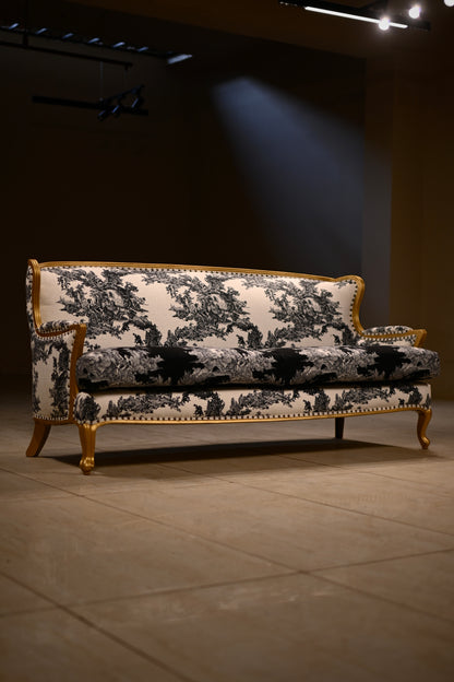 A classic French-style sofa with a black and white toile pattern upholstery and a gold gilded frame, set in a dimly lit gallery or showroom.