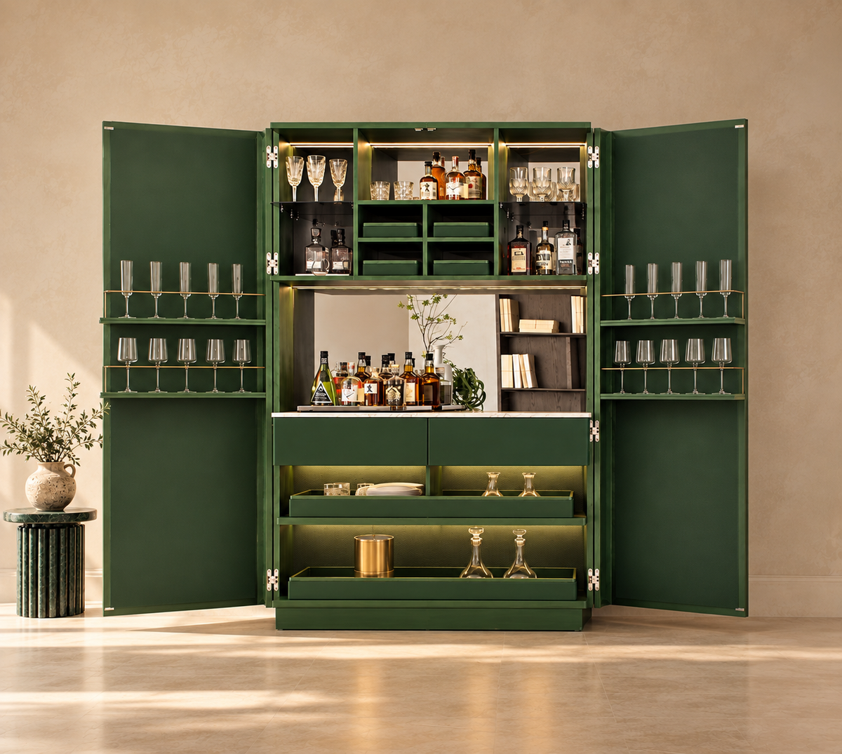 A large dark green bar cabinet with both doors open, styled with bottles, glasses, and bar accessories. The cabinet features multiple shelves, hanging glass holders, a mirrored front, and built-in lighting, set against a warm beige wall and floor.