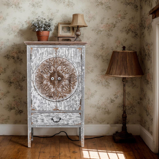 Vintage-style cabinet with decorative door in a room with floral wallpaper and lamps.