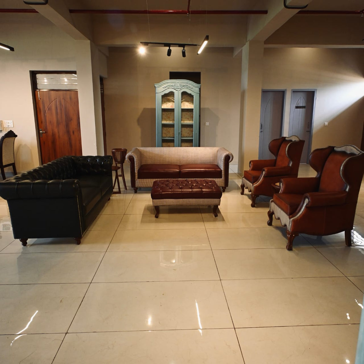 Lounge area with vintage furniture including a black sofa, brown armchairs, and a wooden cabinet.