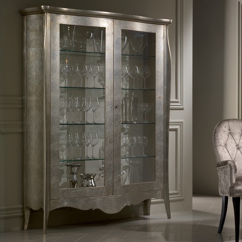 A modern glossy display cabinet with silver detailing, featuring glass doors and shelves with silverware.