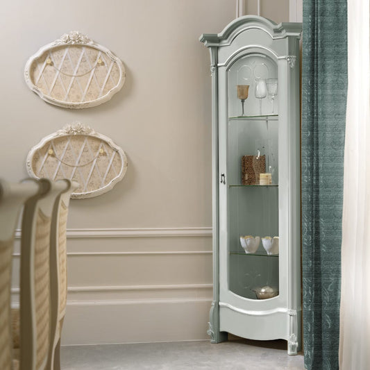A sage pastel colored display cabinet with glass shelves, crafted in a traditional style with elegantly crafted feet, situated in a room with a light interior.