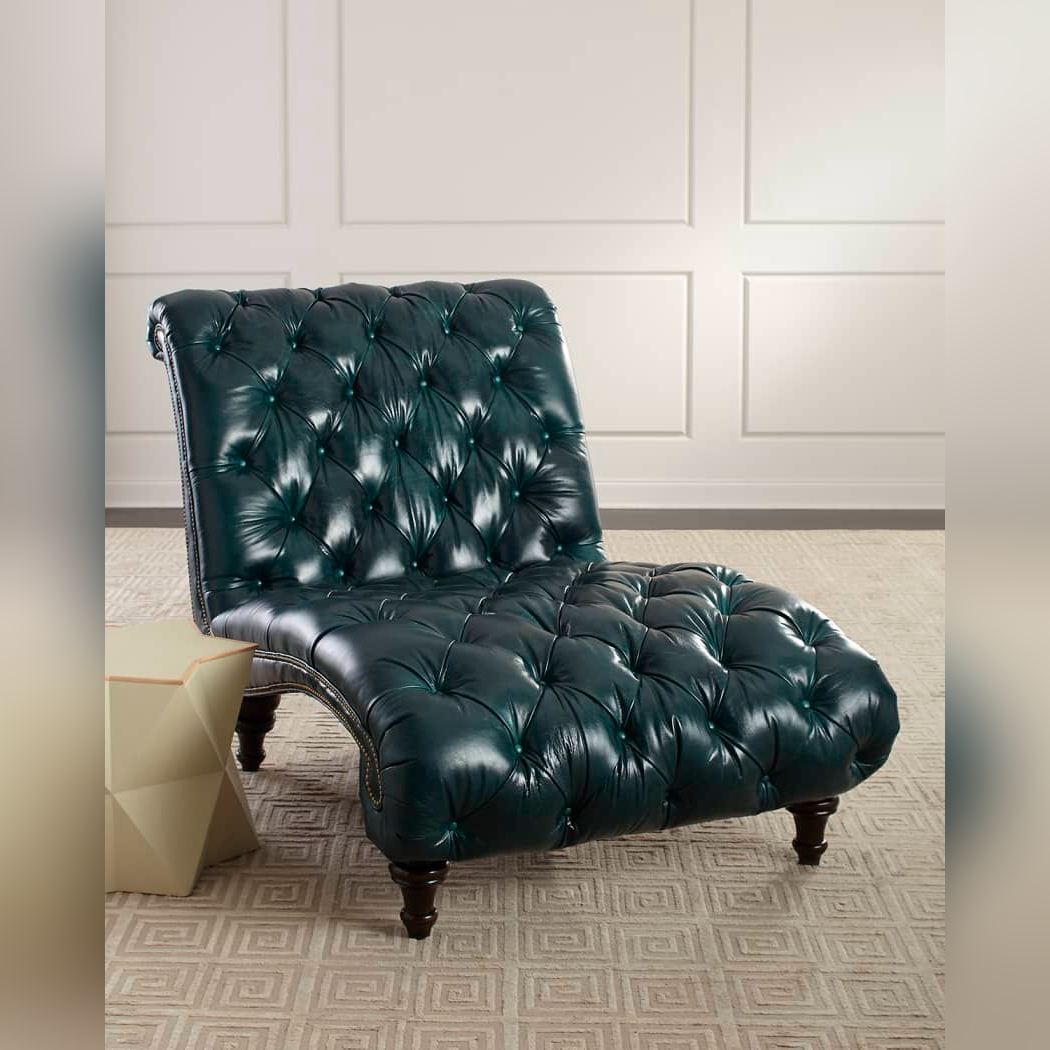 Green leather chaise lounge chair in a room with white paneled walls and a patterned rug.