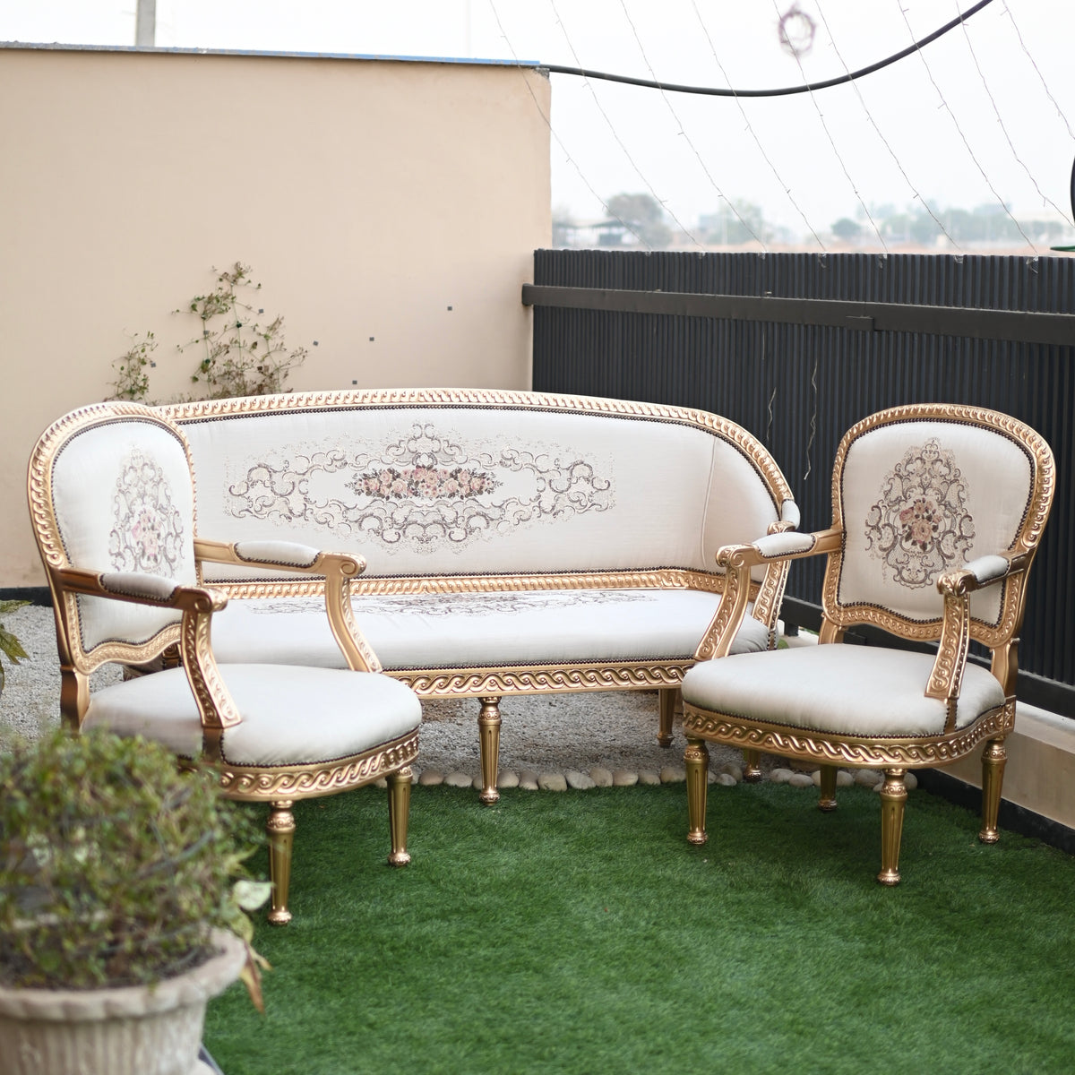 Decorative outdoor furniture set with gold frames and white cushions on a green surface.
