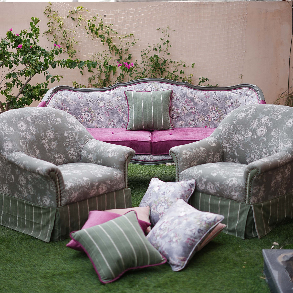 Floral-patterned sofa and armchairs with decorative pillows on a grassy area.