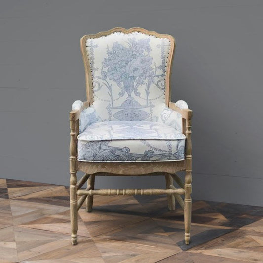 A blue floral armchair with distressed wooden legs and a high backrest, displayed against a grey background.