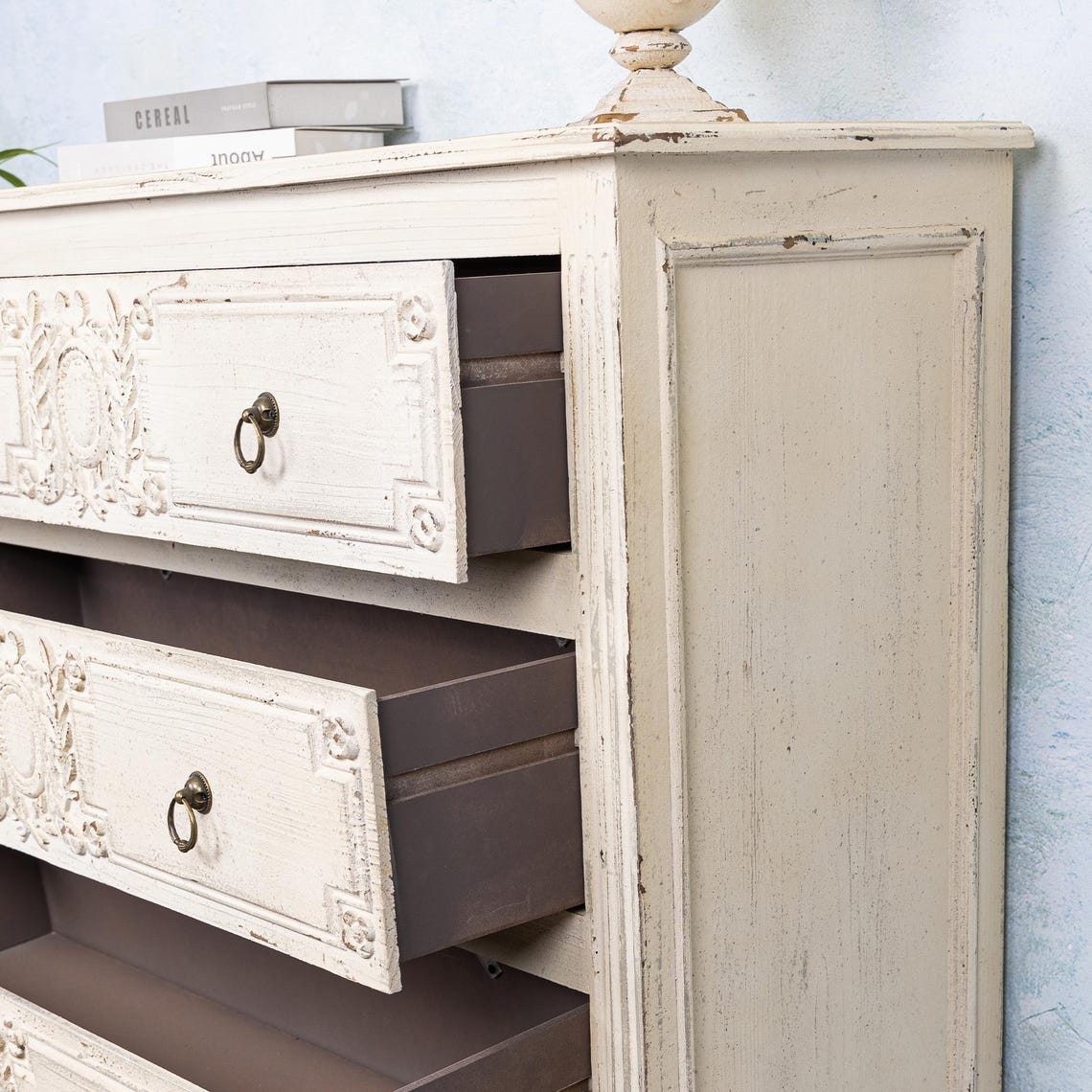 Vintage-style wooden dresser with ornate carvings and open drawers against a light blue wall.
