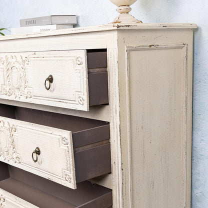 Vintage-style wooden dresser with ornate carvings and open drawers against a light blue wall.