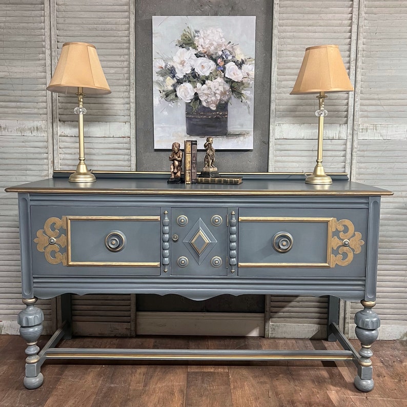 Decorative console table with ornate design, lamps, and artwork in a room.