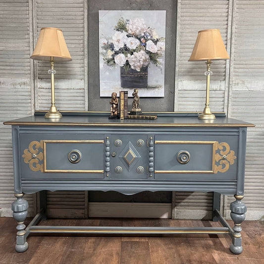 Decorative console table with ornate design, lamps, and artwork in a room.