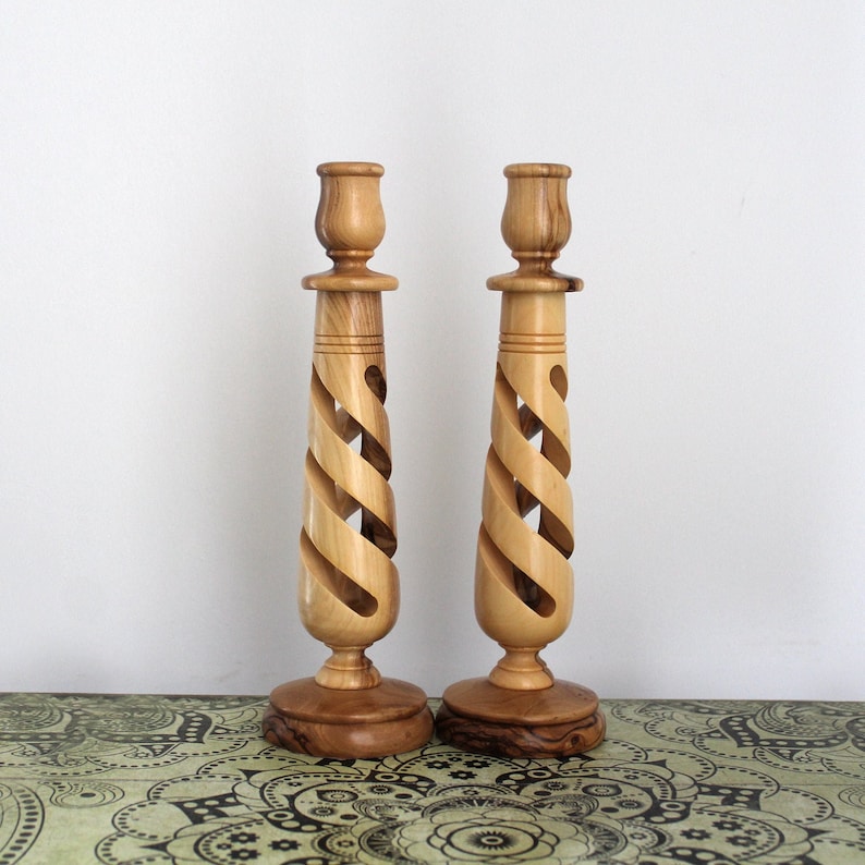 A pair of wooden candle holders with a spiral design and a rose motif at the top, placed on a patterned surface.