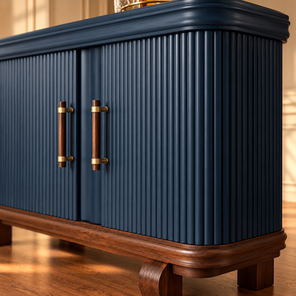 A close-up of a navy blue cabinet with vertical fluted doors, dark wood handles with gold accents, and a dark wood base, set against a warm, softly lit background.