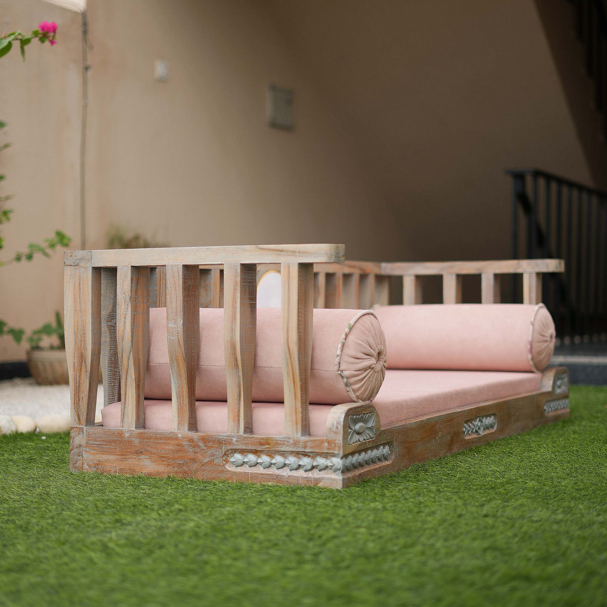 Wooden outdoor sofa with pink cushions on a grassy area