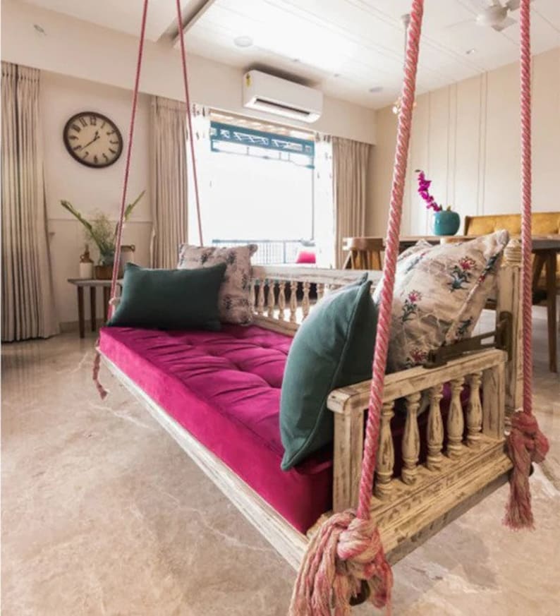 A rustic swing with a magenta seat and green patterned cushions, suspended by pink ropes in an indoor setting.