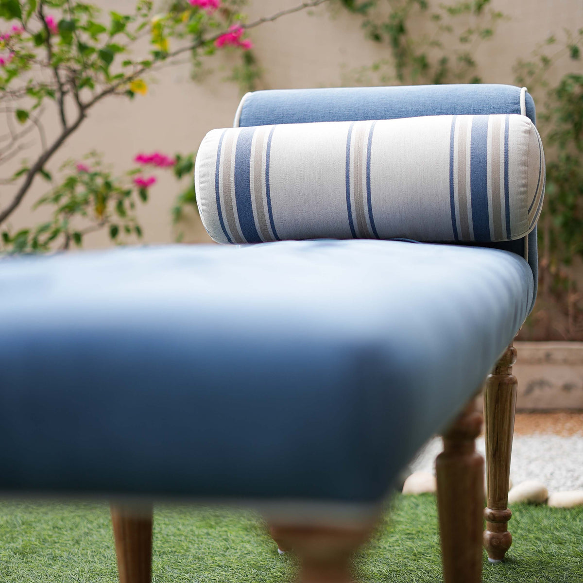 Blue cushioned chair with striped backrest pillow on a grassy area with flowers in the background