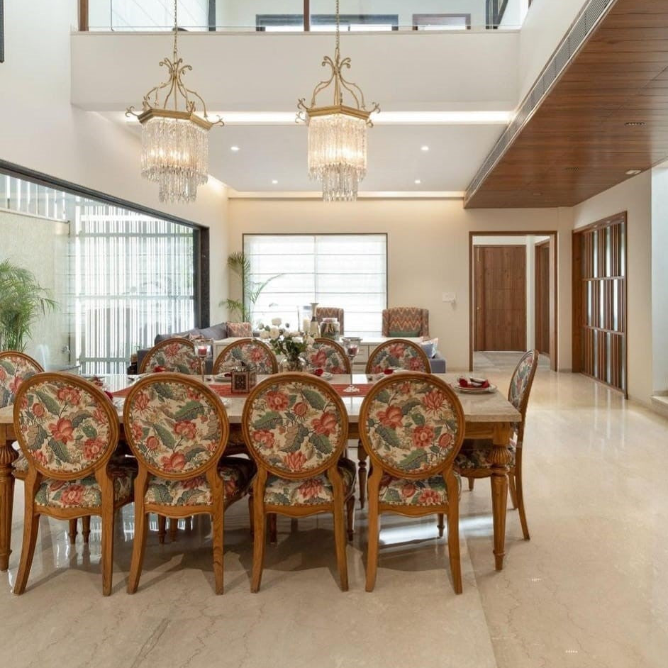 Dining room with floral chairs and a large table, featuring chandeliers and a modern interior design.