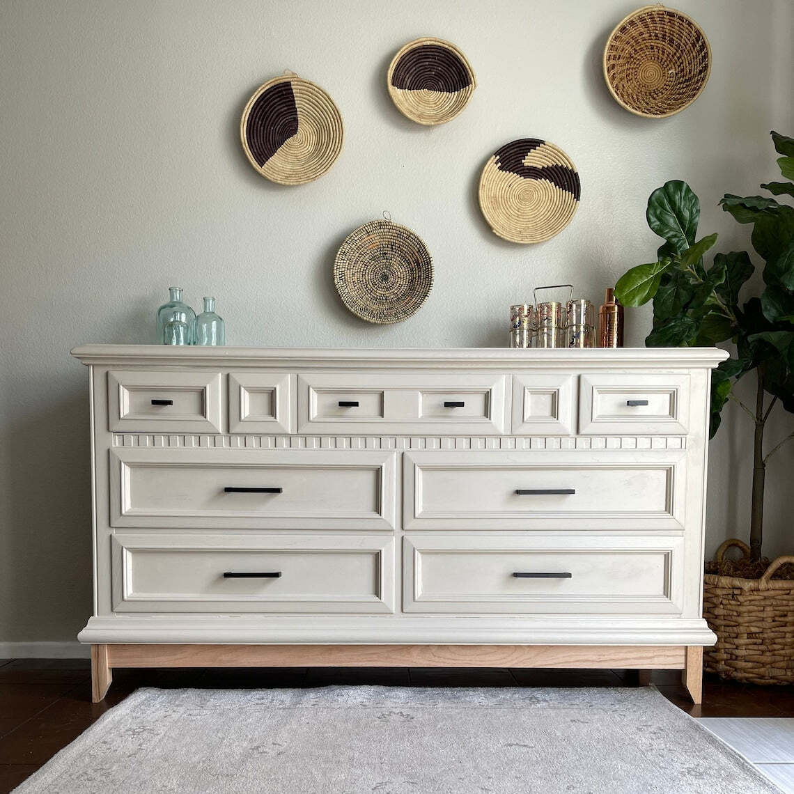 White dresser with wooden legs against a wall with decorative baskets.