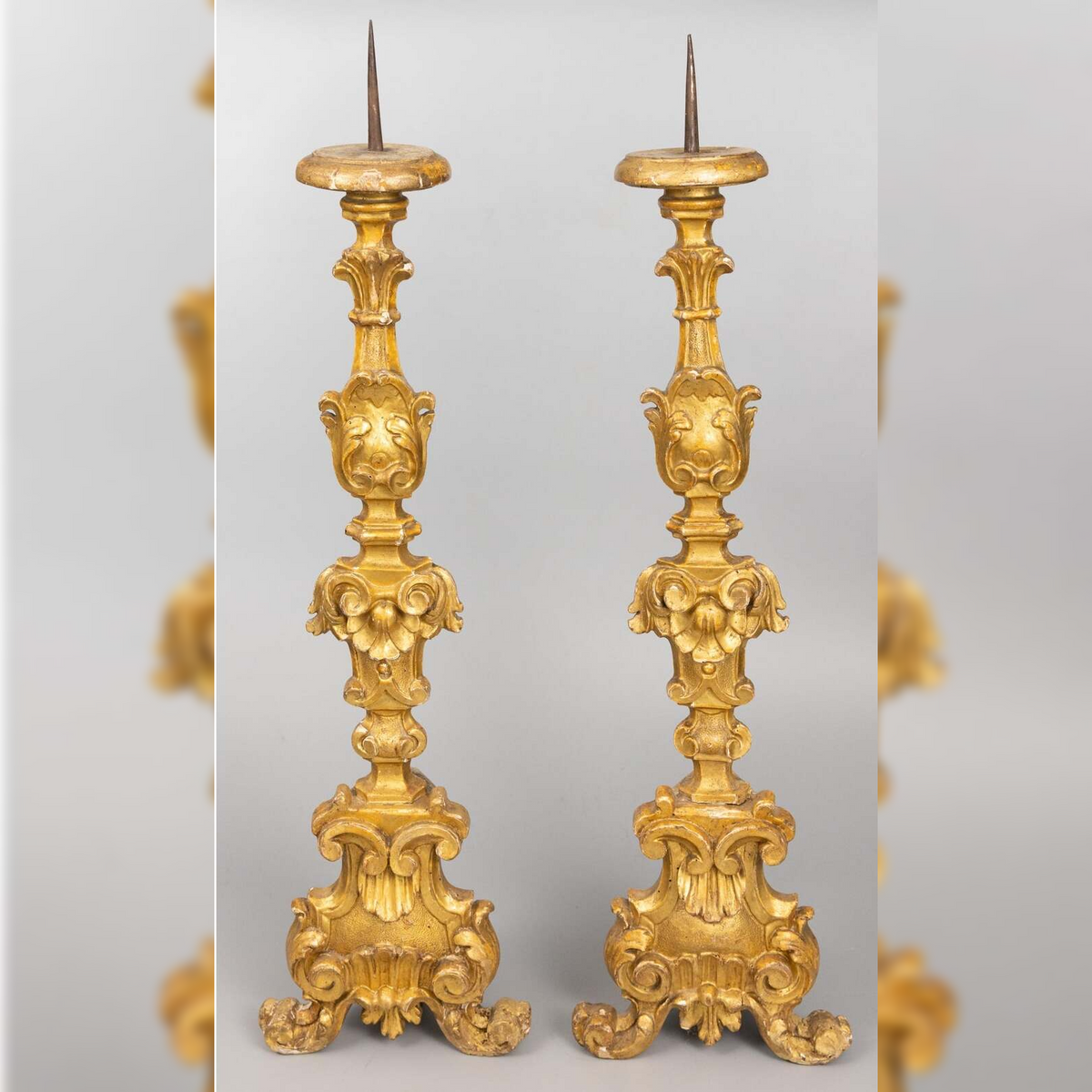 Pair of ornate gold candlesticks on a light gray background