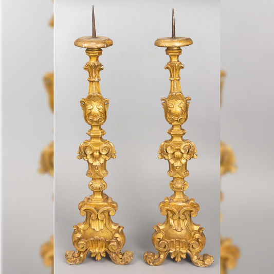 Pair of ornate gold candlesticks on a light gray background