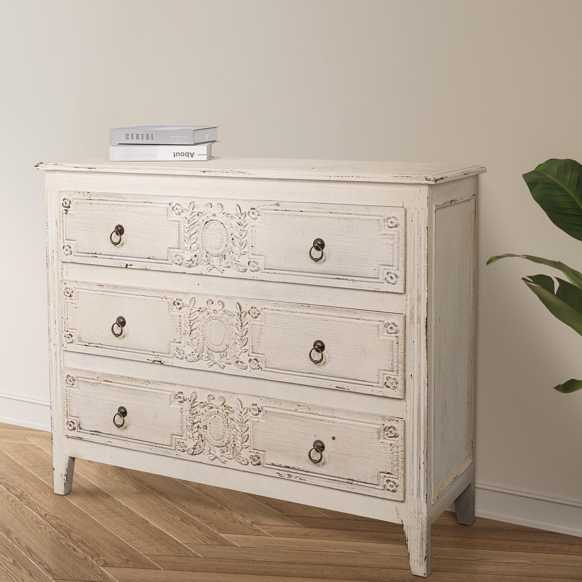 White distressed dresser with decorative carvings on a wooden floor.