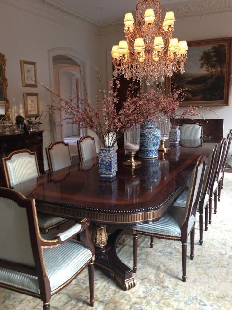 A luxurious 10-seater dining set with dark mahogany wood table and chairs covered in blue silk satin cloth, adorned with gold accents. The room features an ornate chandelier and classic decor.