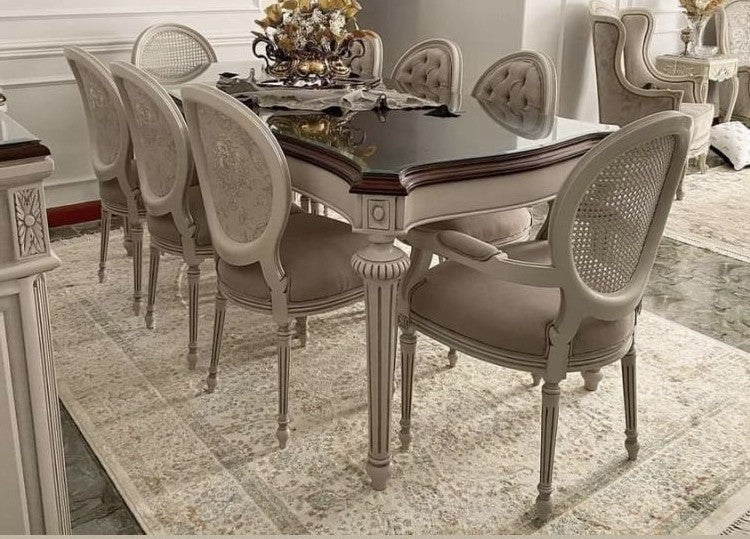 Dining room with a large table and ornate chairs on a patterned rug.