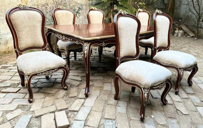 A mahogany dining set with gold accent lines, including a rectangular table and six chairs with upholstered seats, placed on a cobblestone surface.