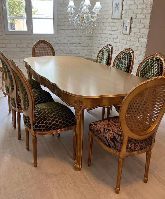 An elegant 8-seater dining set with a gold finish table and chairs with green upholstery, featuring intricate carvings and a geometric pattern.