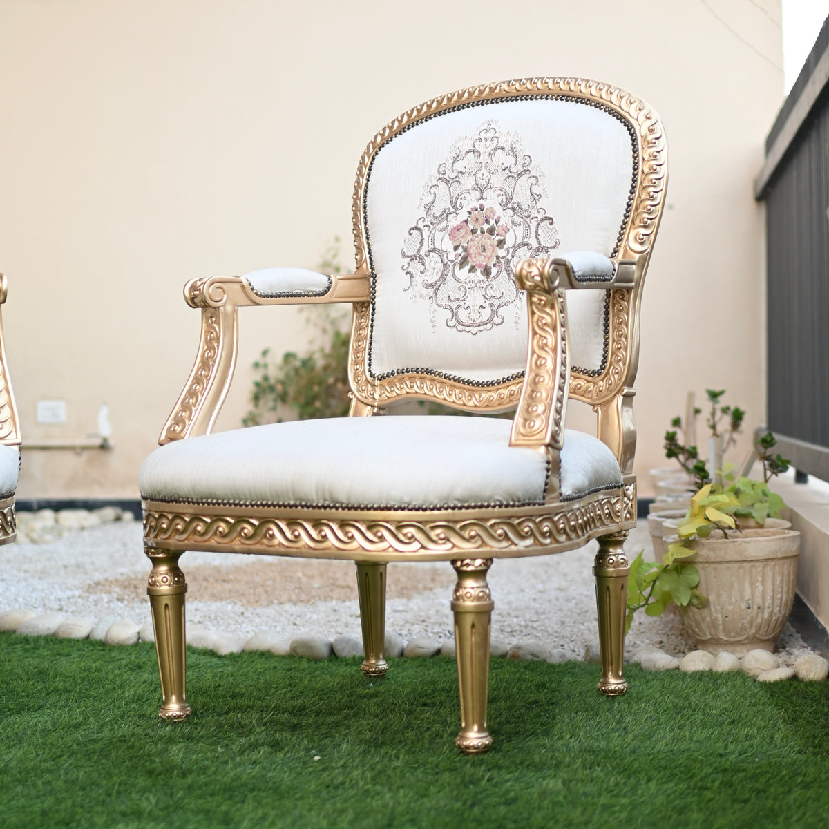 Decorative chair with gold frame and white cushion on a grassy area