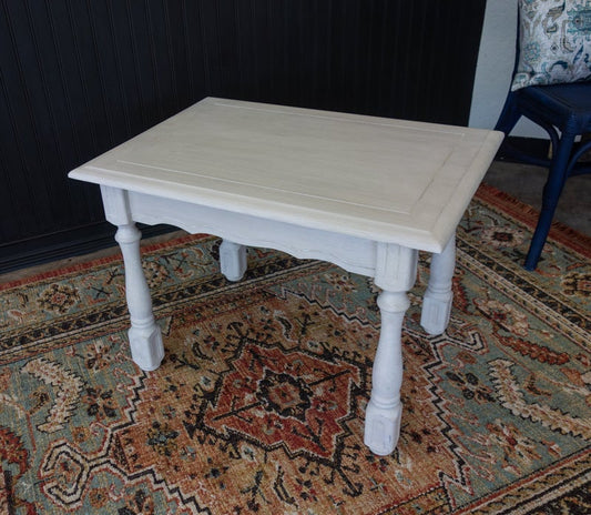 A rectangular ivory French chic table with carved legs on a patterned rug.