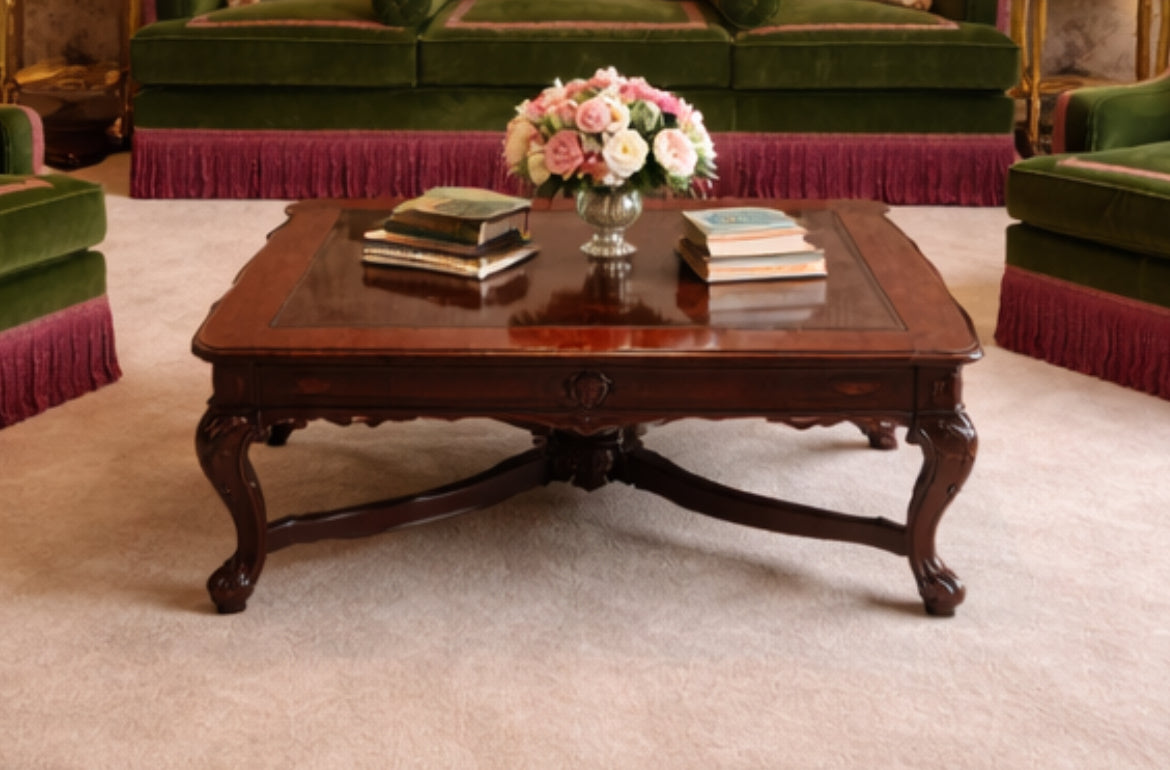 Wooden coffee table with books and a floral arrangement in a room with green velvet chairs.