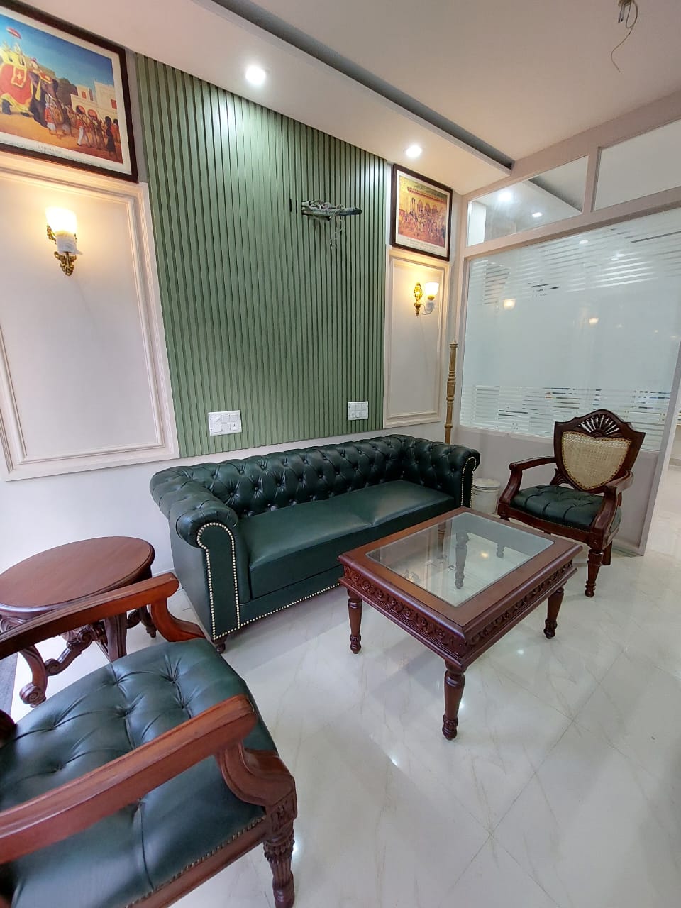Living room with green leather sofa, wooden chairs, and a glass coffee table.