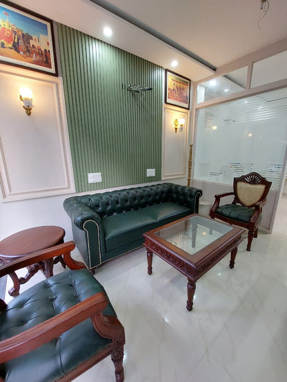 Living room with green leather sofa, wooden chairs, and a glass coffee table.