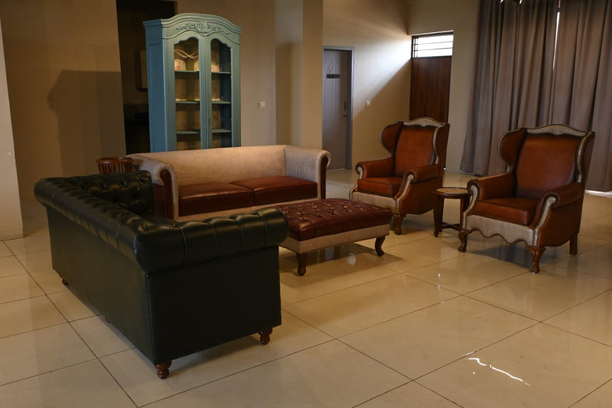Living room with dark green sofa, brown chairs, and ottoman on a tiled floor.