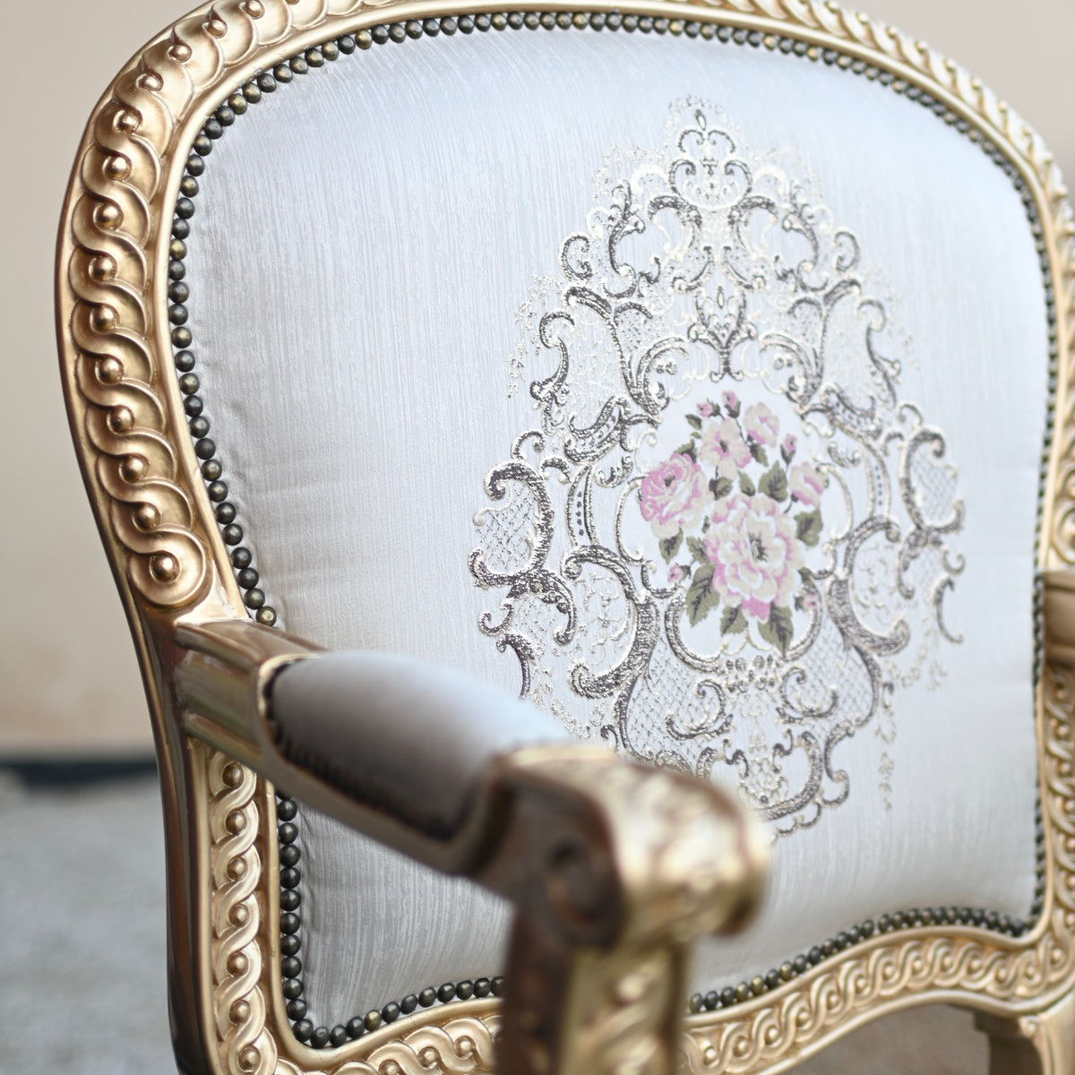 Decorative armchair with intricate gold detailing and floral embroidery on a light background