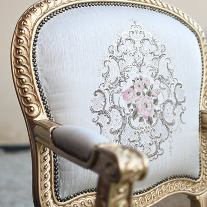Decorative armchair with intricate gold detailing and floral embroidery on a light background
