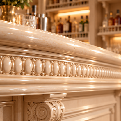 Close-up of an ornate cream-colored carved bar counter with decorative molding and a column detail, set in a warmly lit bar interior with blurred bottles in the background.