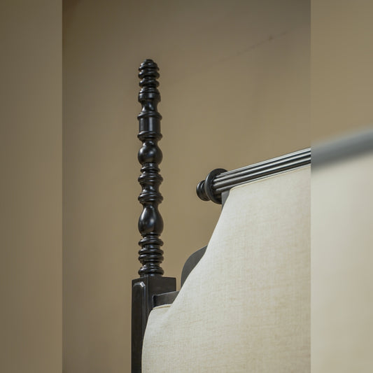 Close-up of a decorative bedpost with a beige pillow against a neutral wall.