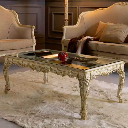 A luxurious French glass-top coffee table with gold-colored metal frame featuring intricate leafy vine carvings, placed on a white furry rug.