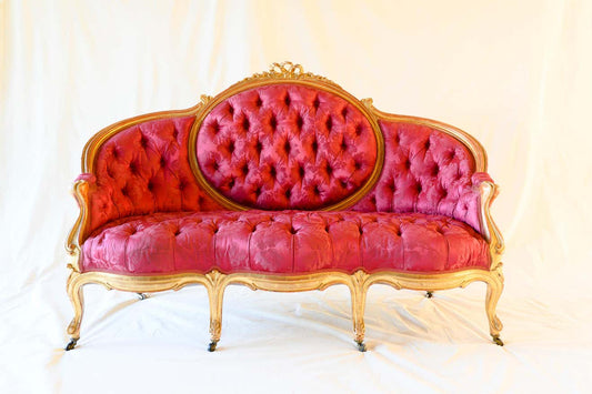 A three-seater crimson sofa with antique gold finish on the frame and tufted upholstery.