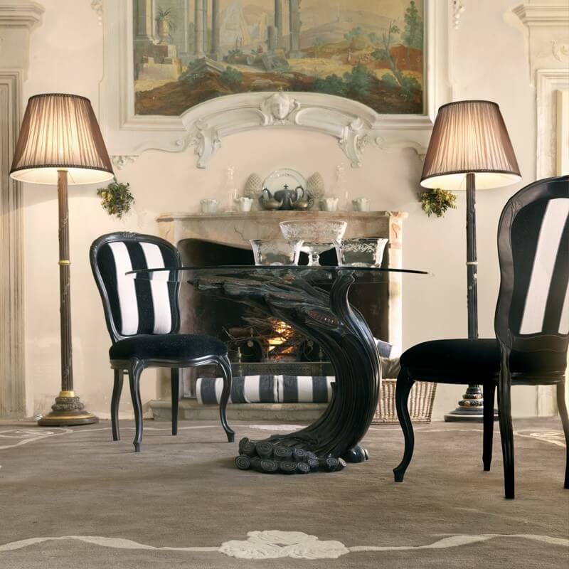 Dining room with a black glass table and striped chairs in front of a fireplace.