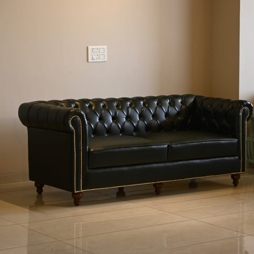 Black leather sofa in a room with beige walls and tiled floor.